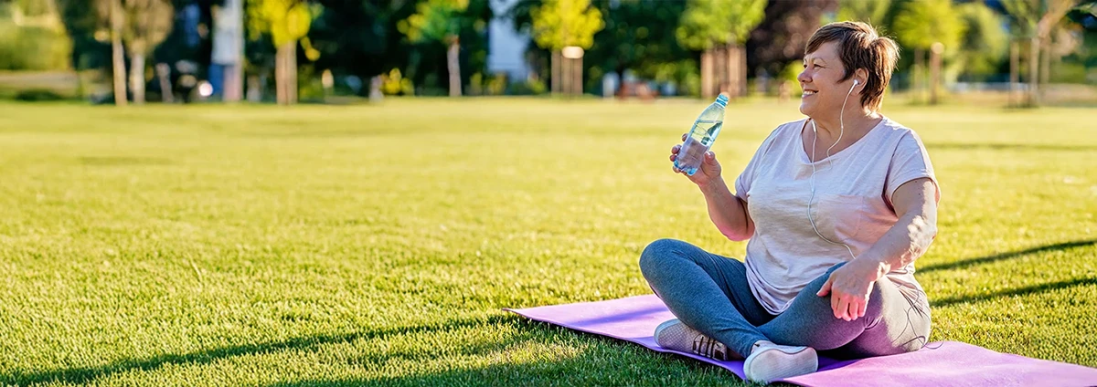 A woman sits on a yoga mat with a bottle of water.
