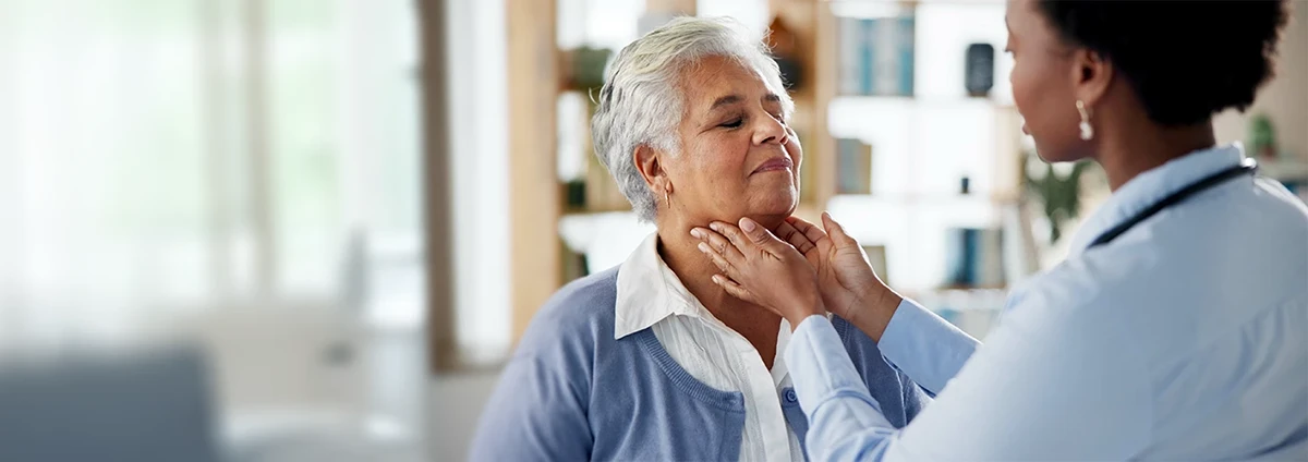 A doctor checks a woman’s throat by placing her hands on it.