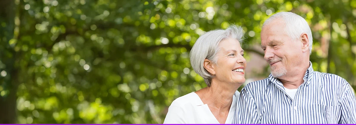 A senior woman and man smile at each other while outdoors.